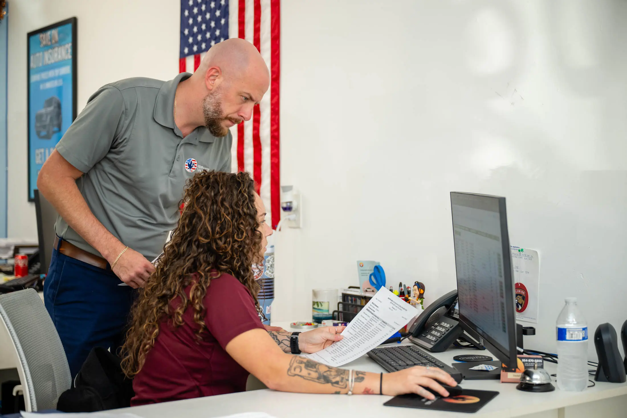 Bearded man assists woman at desk with paperwork.